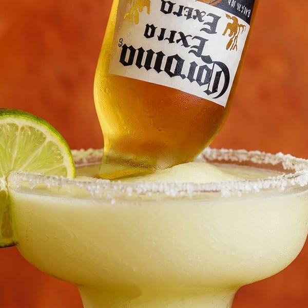 Corona beer bottle inverted into a frozen margarita with a lime wedge and salted rim.