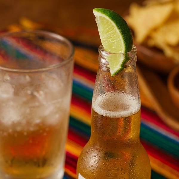 A cold beer with a lime wedge and a glass of ice water on a colorful striped tablecloth.